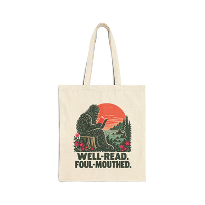 Natural canvas tote with a seated reading Sasquatch, coral California sunset, evergreen coastal scenery, pink wildflowers, and Well-Read. Foul-Mouthed. lettering.